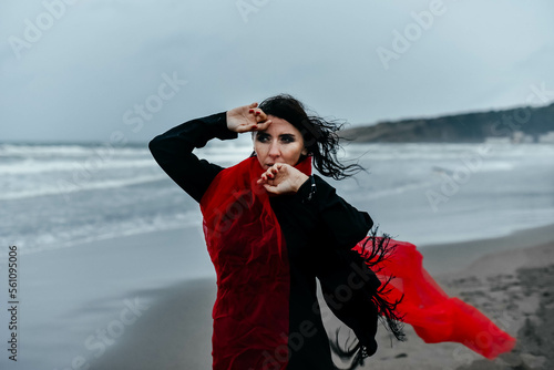 Portrait woman in black dress walking with red scarf on the winter beach