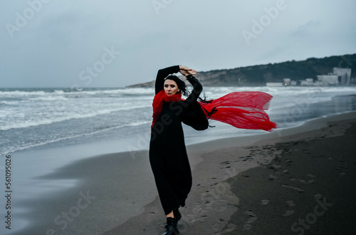 Portrait woman in black dress walking with red scarf on the winter beach
