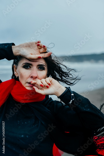 Portrait woman in black dress walking with red scarf on the winter beach