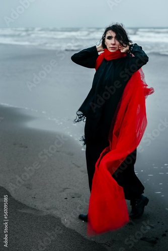 Portrait woman in black dress walking with red scarf on the winter beach