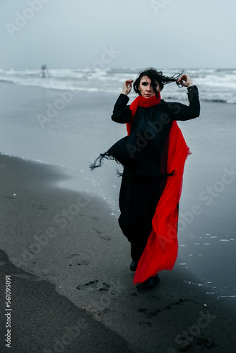 Portrait woman in black dress walking with red scarf on the winter beach