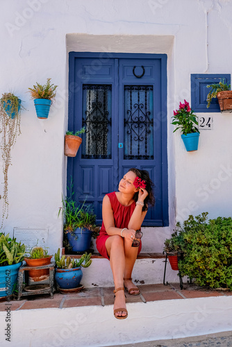 Beautiful woman sitting next to a blue door surrounded by colourful pots with flowers in Frigiliana