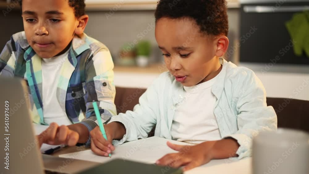 Portrait of cute little kid studying using laptop computer with his older brother at home kitchen Boys doing homework writing exercise in notebook together Distance online education Portrait of cute little kid studying using laptop computer with his older brother at home kitchen Boys doing homework writing exercise in notebook together Distance online education