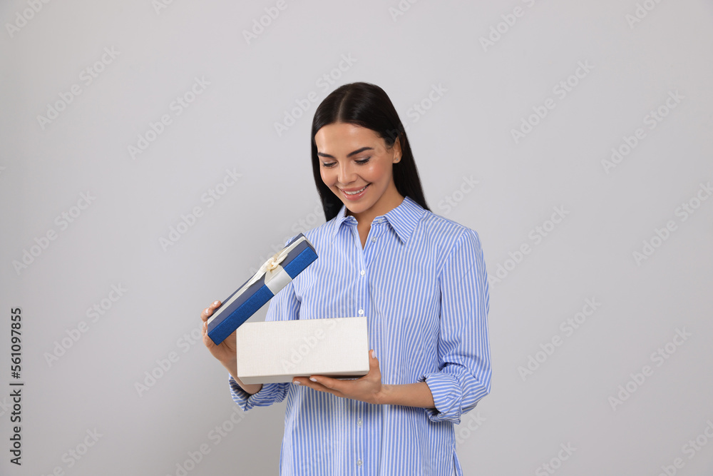 Happy young woman opening gift box on light grey background Happy young woman opening gift box on light grey background