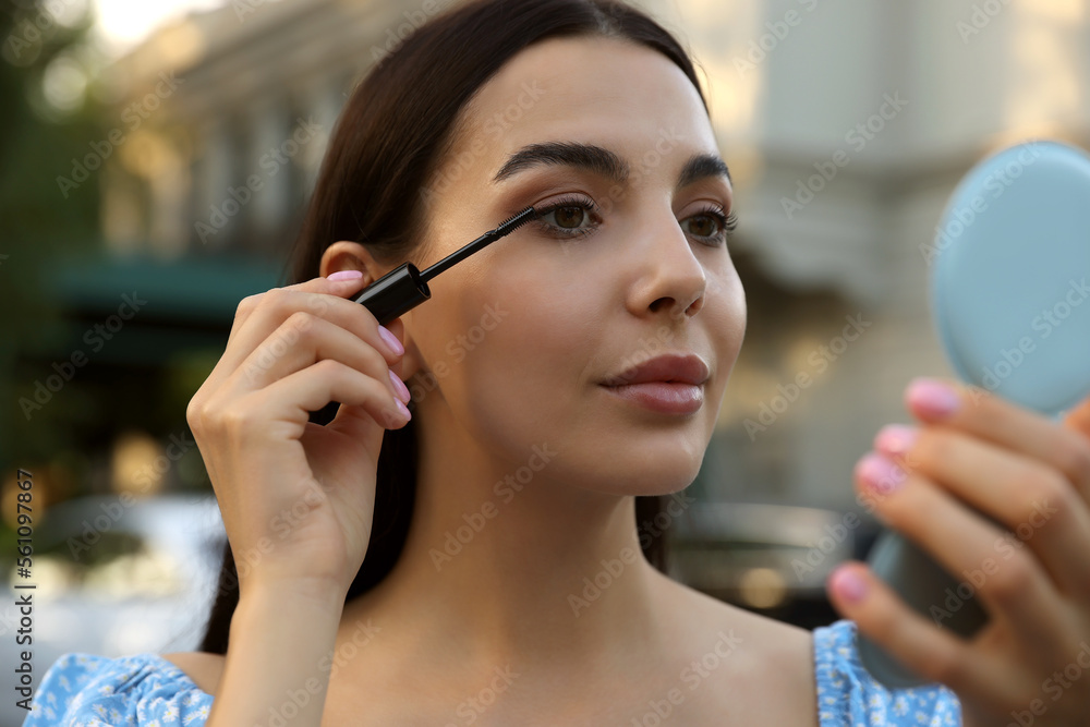 Beautiful woman with cosmetic pocket mirror applying mascara outdoors, closeup Beautiful woman with cosmetic pocket mirror applying mascara outdoors, closeup