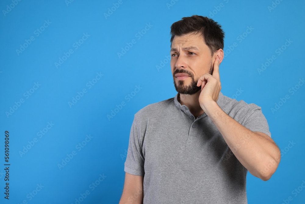 Man suffering from ear pain on light blue background, space for text Man suffering from ear pain on light blue background, space for text