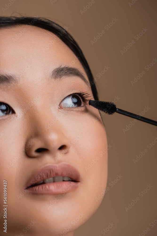 Cropped view of asian woman with makeup holding mascara applicator isolated on brown.