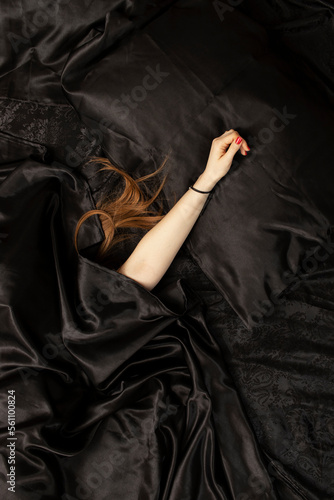 Female red hair and a hand on black bed sheet. Sleeping concept.