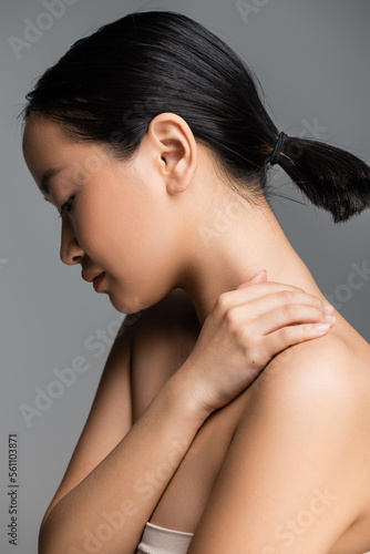side view of asian woman with ponytail posing with hand on naked shoulder isolated on grey.