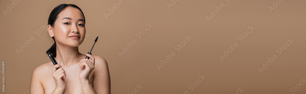 Young asian woman with naked shoulders holding mascara isolated on brown, banner. Young asian woman with naked shoulders holding mascara isolated on brown, banner.