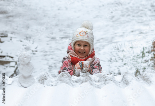 Child walking outdoors on a winter snowy day.  The little girl plays snowballs and a snowman.