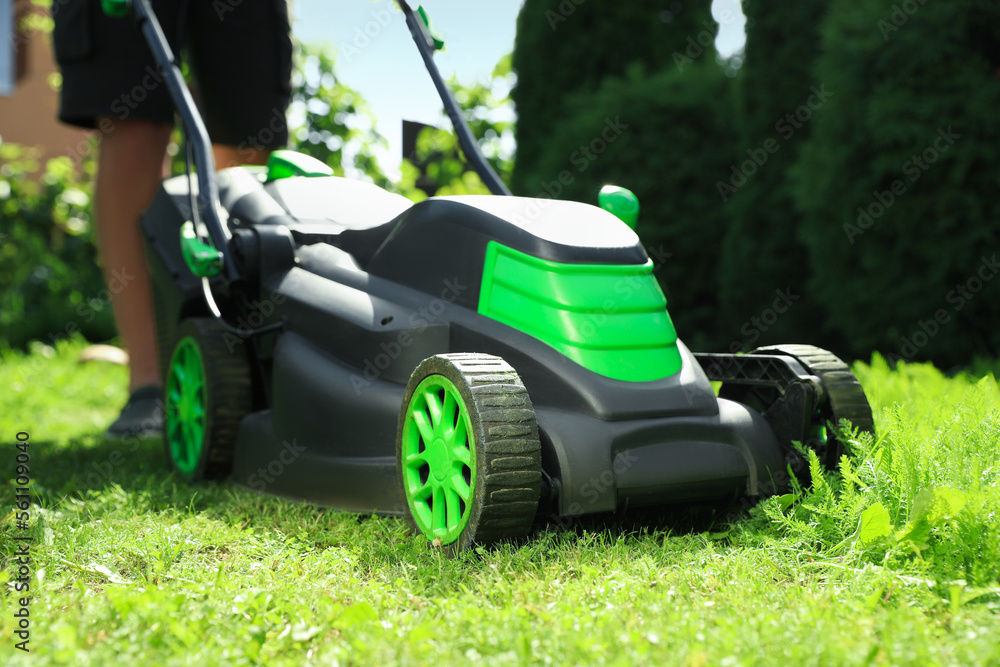 Man cutting grass with lawn mower in garden on sunny day, closeup Man cutting grass with lawn mower in garden on sunny day, closeup