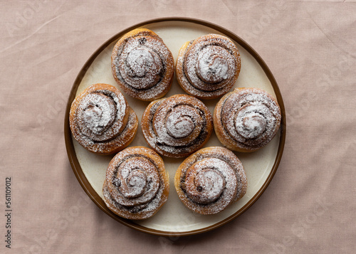 Freshly baked cinnamon rolls sprinkled with powdered sugar on parchment paper. Sweet homemade Christmas baking. . Kanelbule is a Swedish dessert. photo