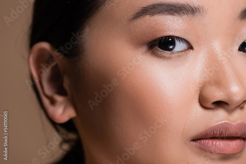 Cropped view of young asian woman looking at camera isolated on brown.