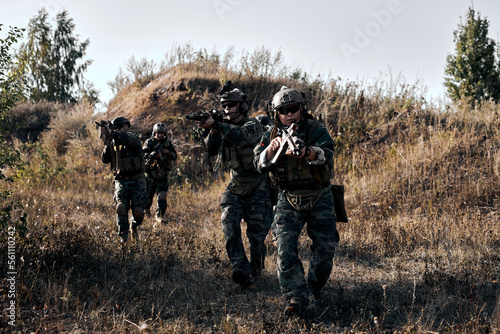 Team of army soldiers outdoors, marines group in action, shooting with weapon and machine gun, attacking enemy. Young caucasian men in military uniform concentrated on fight