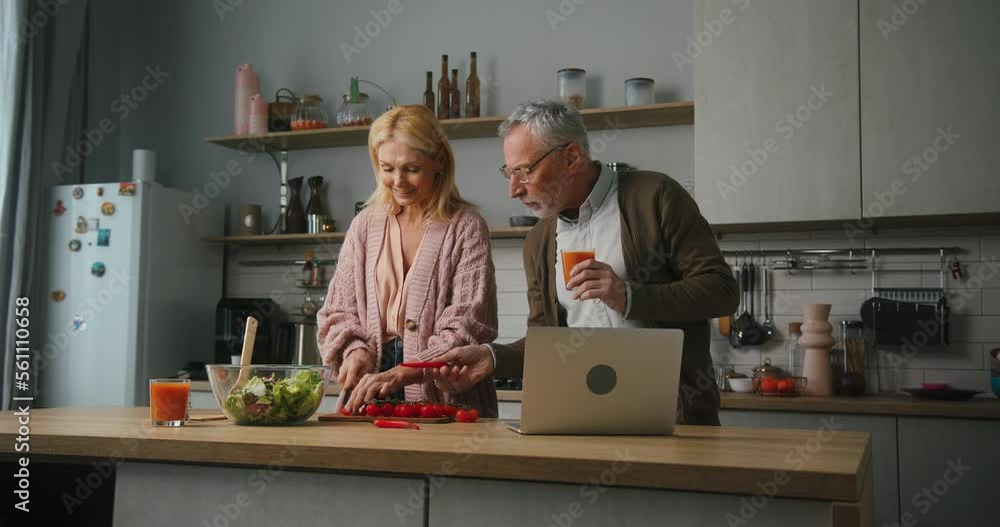 Woman cooks salad while husband finishes work on laptop Woman cooks salad while husband finishes work on laptop