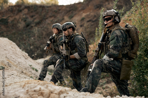 Group of armed special forces soldiers with rifles standing together looking at side, planning strategy of shooting, waiting for enemy. confident serious soldiers in military clothes outdoors