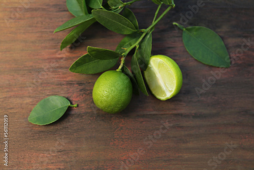 Branch with fresh leaves and limes on wooden table, closeup