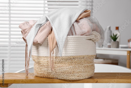 Wicker laundry basket with clothes on wooden tray in bathroom