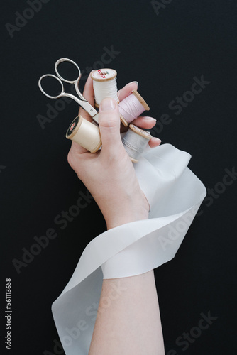 Sewing supplies and silver scissors and a natural white silk ribbon in woman hand against black background. photo