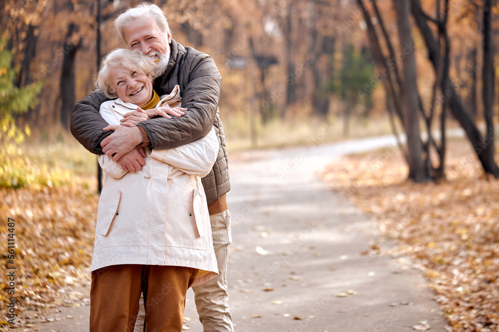 Fototapeta premium Joyful Friendly Senior Elderly Couple In Coats Enjoy The Walk Together, Hugging, Laughing. Caucasian European Married Man And Woman In Love, During Autumn Season. Happiness, Lifestyle Concept