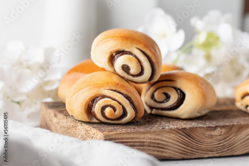 Sweet cinnamon buns on wooden board with white spring flowers. Easter traditional pastry food