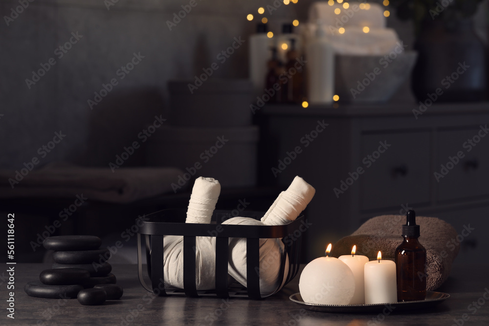 Herbal massage bags, burning candles and stones on grey table. Spa products