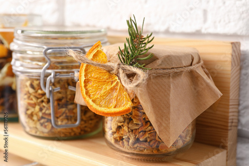 Jars of dried orange zest seasoning on wooden shelf near white brick wall