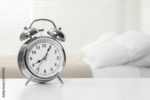 Silver alarm clock on white wooden table in bedroom, space for text