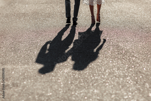 Shadows of a young couple walking down the street holding hands. Bright sunny day. Newlyweds go far away in sun lights. Tenderness, love and relationship.