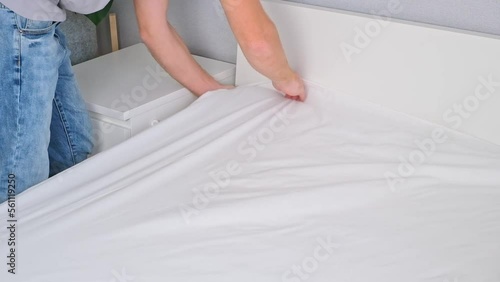 A man makes his cozy bed with fresh bright white bed linen. Making the bed with fresh bed linen by man. The day of the change of bedclothes.