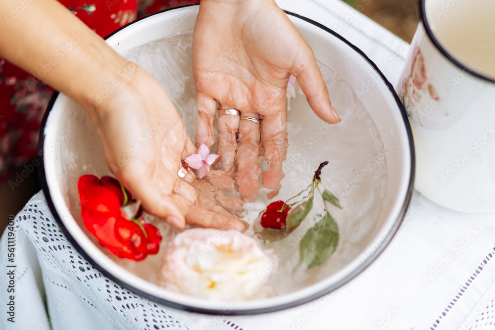 closeup view of woman soaking her hands and in dish with water and flowers on. Spa treatment and product for female and hand spa. orchid flowers in ceramic bowl.