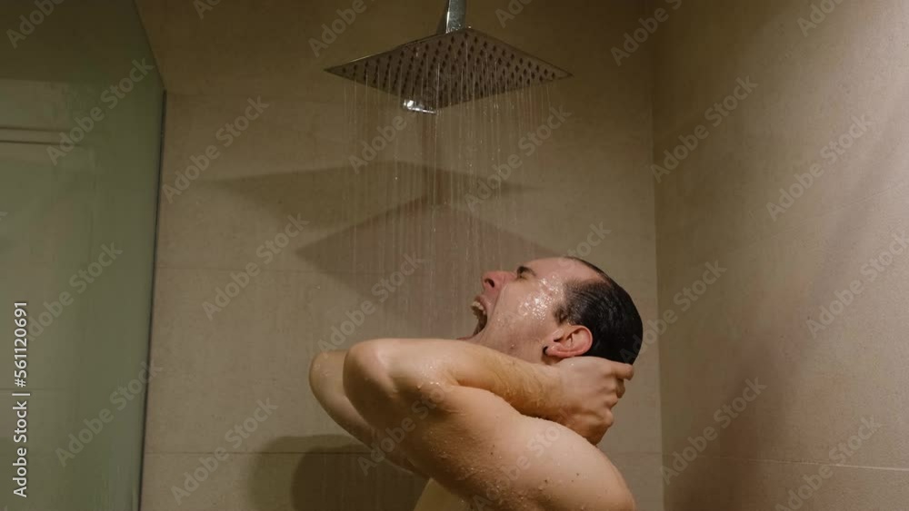 An upset angry man in a shower screaming and learning against a glass