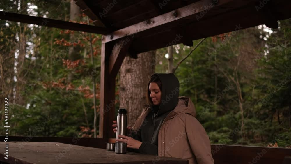 a woman tourist drinks tea from a thermos in a gazebo in the forest a woman tourist drinks tea from a thermos in a gazebo in the forest