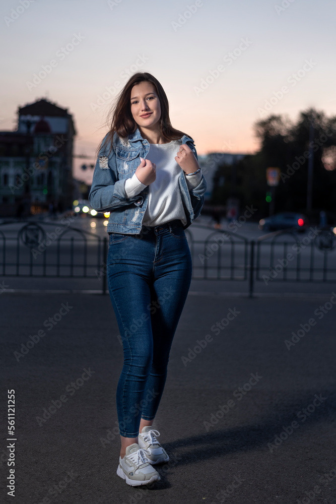 Young stylish girl on evening city background. Young woman walking in city street, summer time