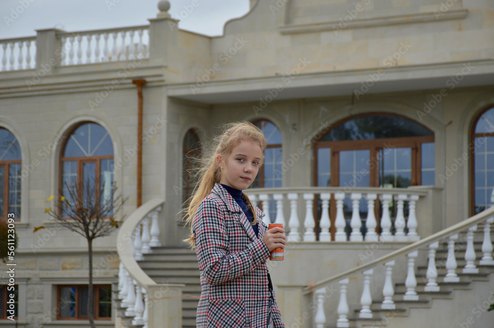 a beautiful girl in a plaid coat on a walk in the autumn park against the backdrop of a vintage building, holding a can of drink in her hand. quench your thirst in the fresh air. active lifestyle