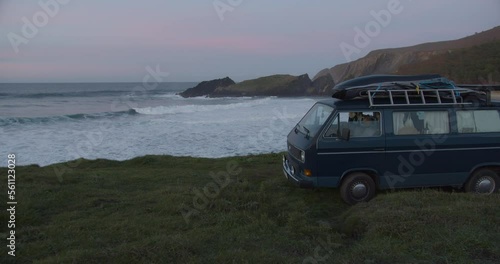 Camper van parking at the cliffs in a lonely bay during blue hour after sunset while big waves are rolling in the background in Galicia, Spain