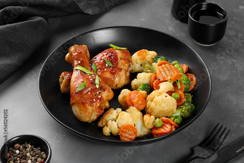 Roasted Baked chicken legs drumsticks with vegetables on black plate on dark background. Meal, dinner diet concept, diet.