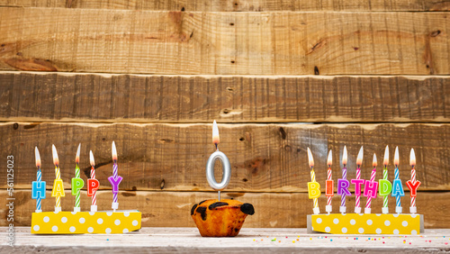 Muffin with a burning candle background for the anniversary on a beautiful wooden background. Postcard with letters of candles with congratulations for the holiday before the birthday.  Copy space 0 photo