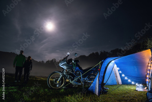 Camping, blue tent with light, touring motorcycle for travel. The concept of recreation and tourism. Space for text, selective focus. Mist, fog and moonlight. Couple man and woman.
