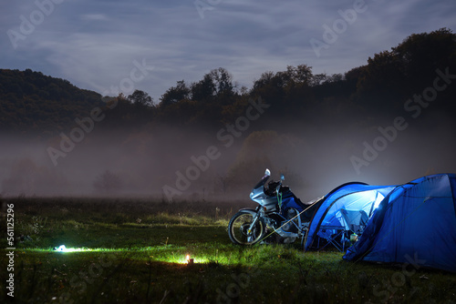 Obraz na płótnie Camping, blue tent with light, touring motorcycle for travel. The concept of recreation and tourism. Space for text, selective focus. Mist, fog and moonlight. w salonie