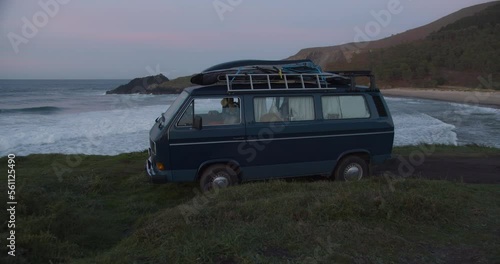 Camper van parking at the cliffs in a lonely bay during blue hour after sunset while big waves are rolling in the background in Galicia, Spain