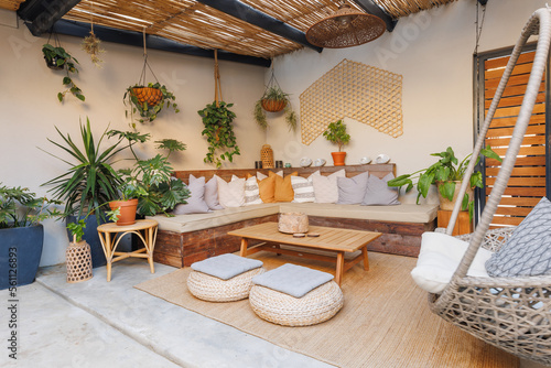 Houseplants hanging on wall and multicolored cushions arranged on sofa with table and stools