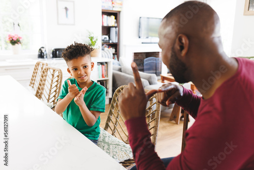 Happy african american father and son at table, talking in sign language photo
