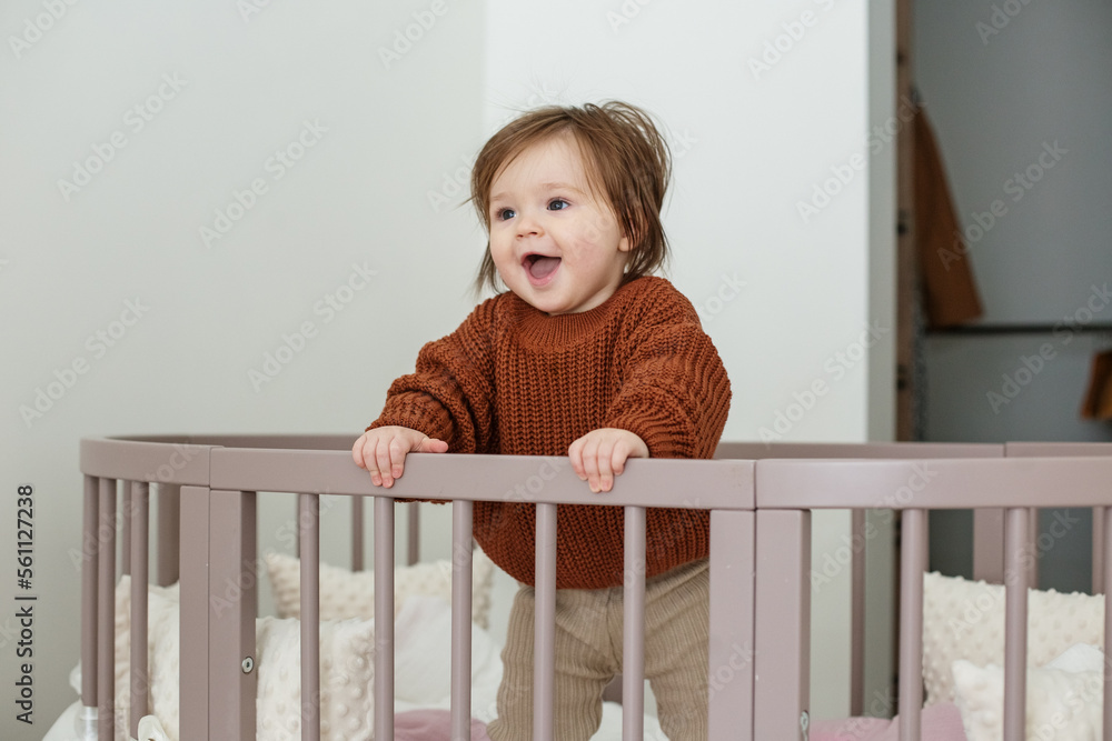 Cute laughing baby standing in round bed. Little girl learns to stand in her crib. Cute laughing baby standing in round bed. Little girl learns to stand in her crib.