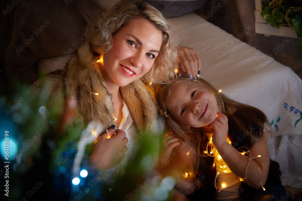 Cute mother and daughter in a room with Christmas garlands. The tradition of decorating the house and dressing up for the holidays. Gifts for the family. Happy childhood and motherhood