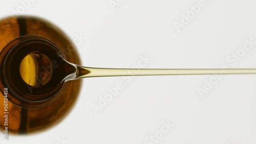 Vertical macro shot of brown reagent bottle is being tilted and yellow oil pours from it on grey background | Abstract anti-wrinkle cosmetics ingredients formulating concept
