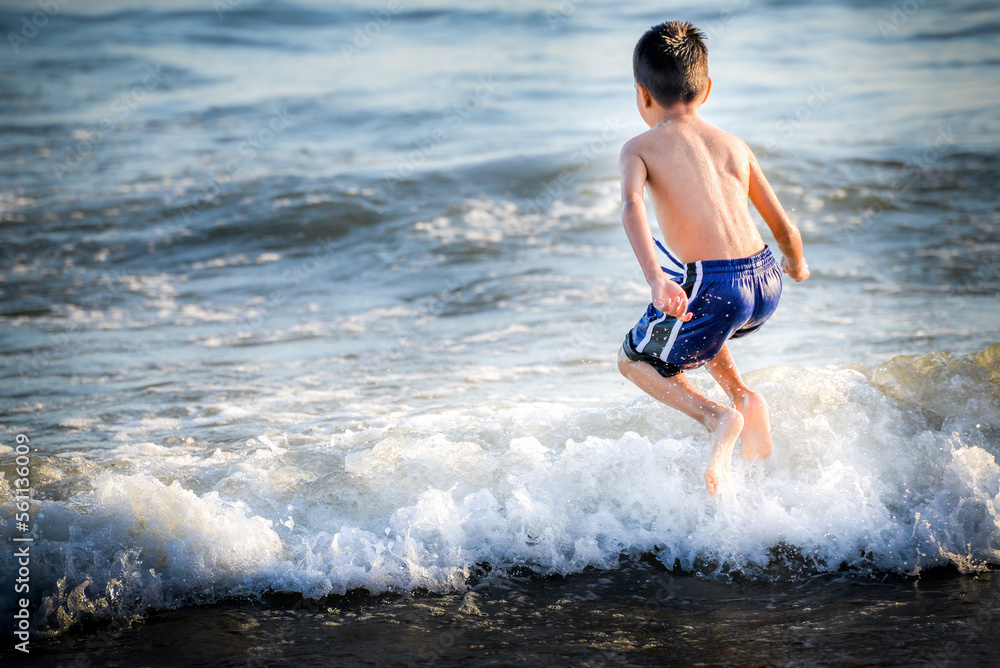 Young boy jumps over a wave and into the Pacific Ocean in Santa Monica, California