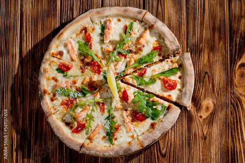 Pizza with salmon, mozzarella, cherry tomatoes, arugula, lemon and parmesan. Italian cuisine on a woden background