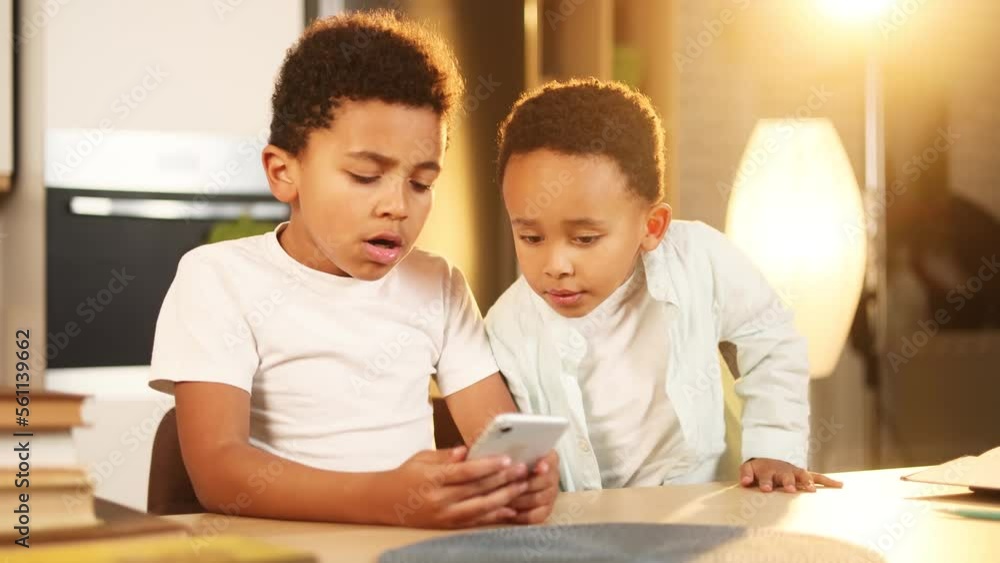 Adorable cute african american little boys brothers hold smartphone scrolling social media use educational children app application having fun with mobile phone gadget or play game together at home Adorable cute african american little boys brothers hold smartphone scrolling social media use educational children app application having fun with mobile phone gadget or play game together at home